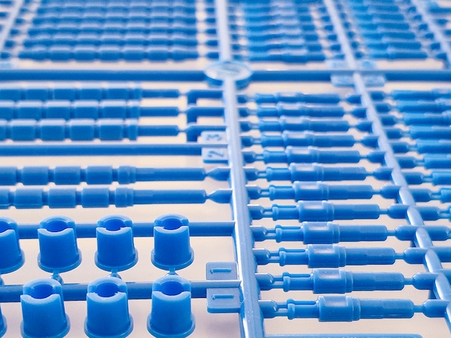 Polyethylene plastic injection molded parts arranged in a production grid, illustrating flexible, chemical-resistant thermoplastic used in packaging and industrial products